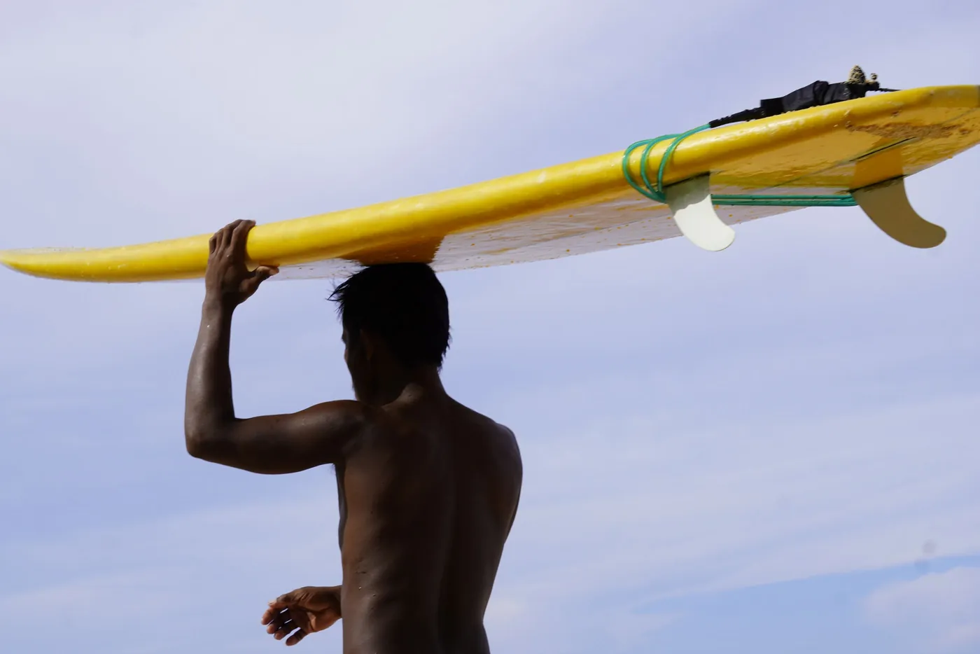 Photo: Kat Carabio (Pexels License) A surfer carrying a yellow surfboard over his head on a sunny day in Caraga, the region Siargao belongs to
