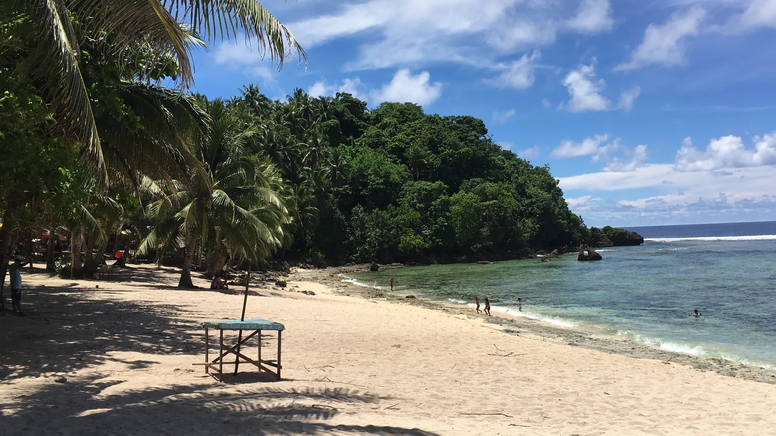 Photo: ChaasPrime (CC BY-SA 4.0) Palm trees shading a sand beach beside a shallow turquoise reef on Siargao Island, Philippines